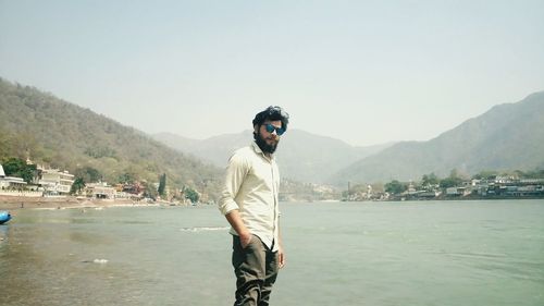 Portrait of man with hand in pocket standing against river during foggy weather