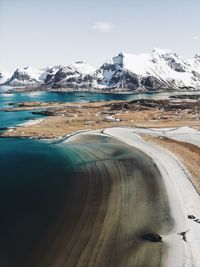 Scenic view of sea by snow covered mountains against sky