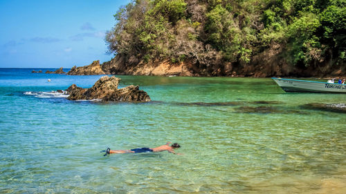 Man lying on rock in sea against sky