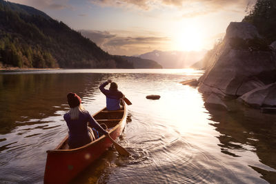 Rear view of women sitting on lake against sky