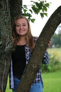 Portrait of smiling teenage girl standing by tree trunk at field