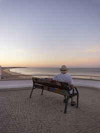 Portugal, senior man siting on bench watching sunrise