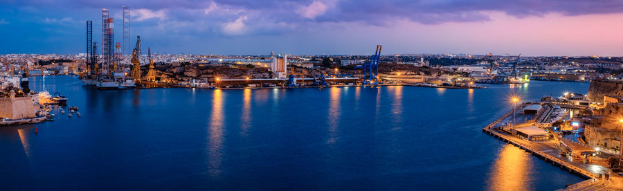 Panoramic view of illuminated city by sea against sky