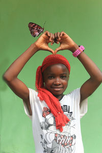 Portrait of young woman with arms raised standing against wall