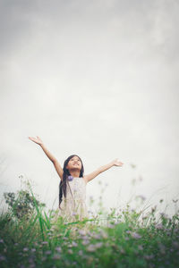 Woman with arms raised on field against sky