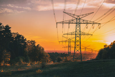 Trees and electricity pylon against sky during sunset