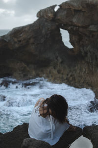 Rear view of woman standing on rock at beach