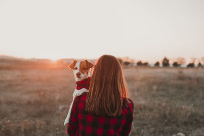 Woman with dog standing on field during sunset