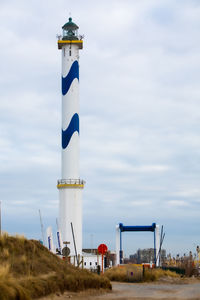 Lighthouse by building against sky