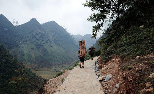 Rear view of people walking on village road against cloudy sky