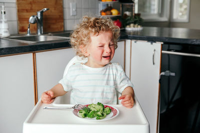 Crying caucasian kid boy with broccoli on plate.  toddler screaming in tantrum. terrible two. 