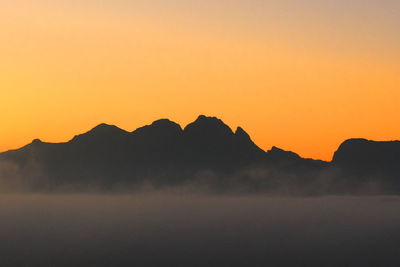 Scenic view of silhouette mountains against orange sky
