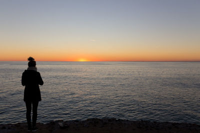 Rear view of man standing on beach during sunset