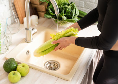 Midsection of woman washing celery in kitchen sink