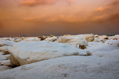 Close-up of snow on shore against sky during sunset