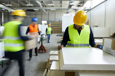 Worker examining wooden boards in factory with colleagues moving in background