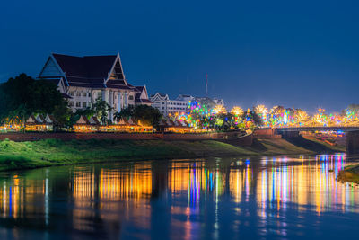 Illuminated buildings by river against sky at night