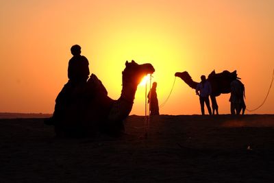 Silhouette people at desert against sky during sunset