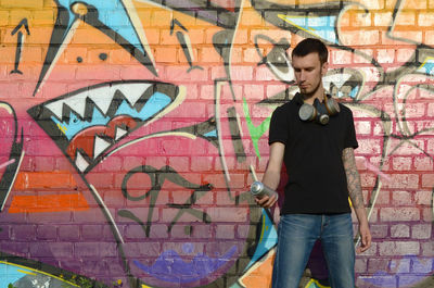 Full length of young man standing against graffiti wall