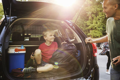 Happy father looking at boy sitting in car trunk