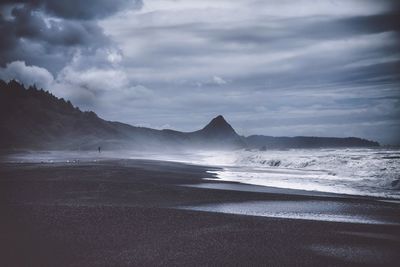 Scenic view of beach against cloudy sky