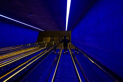 Low angle view of woman standing on illuminated escalator