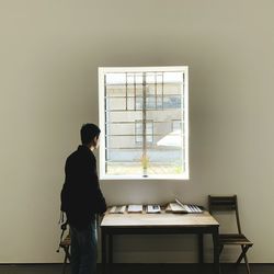 Rear view of man standing by window at home