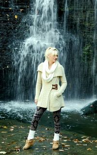 Full length of a young woman standing against waterfall