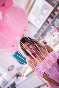 Happy woman holding pink helium balloons while standing in store