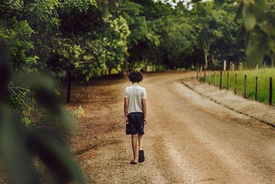 Rear view of boy walking on road by trees