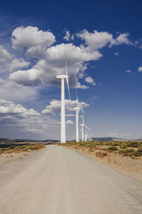 Wind turbines by cloudy sky at wind farm