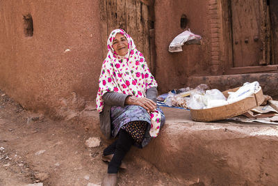 Portrait of senior woman wearing hijab sitting outside house