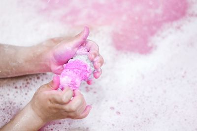 Cropped hands of woman holding sponge while taking bubble bath in bathtub