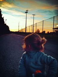 Girl riding bicycle on street against sky at sunset