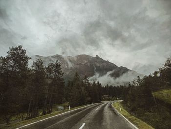 Country road by mountains against sky