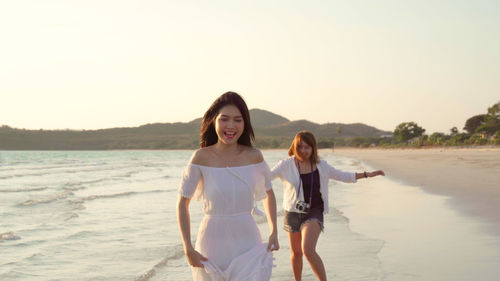 Cheerful women walking on beach against sky