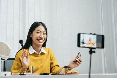 Portrait of smiling young woman using phone on table