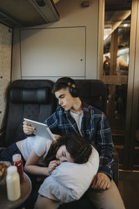 Boy using tablet pc with sister resting on lap in train