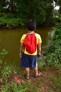 Rear view of boy standing by lake against trees