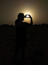 Rear view of silhouette man standing on field against sky during sunset