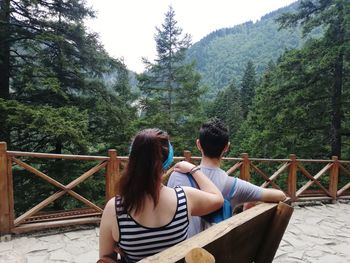 Rear view of people sitting on bench in forest