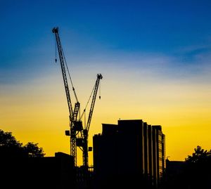 Silhouette crane by building against sky during sunset