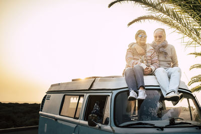 Senior couple sitting on camper van against clear sky