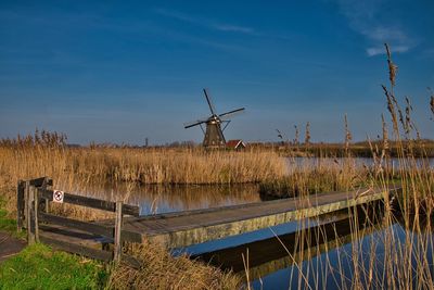 Traditional windmill on field by lake against sky