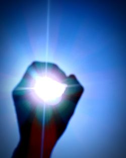 Close-up of hand holding illuminated light against blue sky
