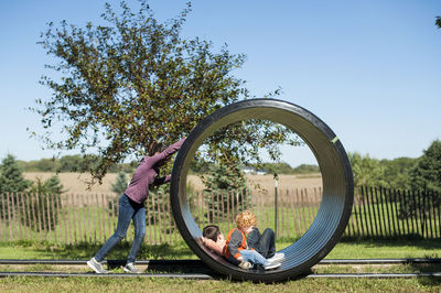 Sister pushing large pipe with brothers in it at pumpkin patch