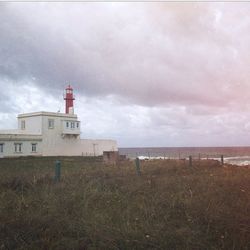 Lighthouse on beach against cloudy sky