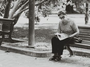 Full length of woman reading book while sitting on bench in park