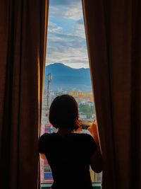 Rear view of woman looking through window at home