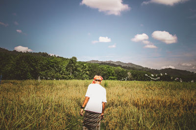 Rear view of man walking in farm against sky